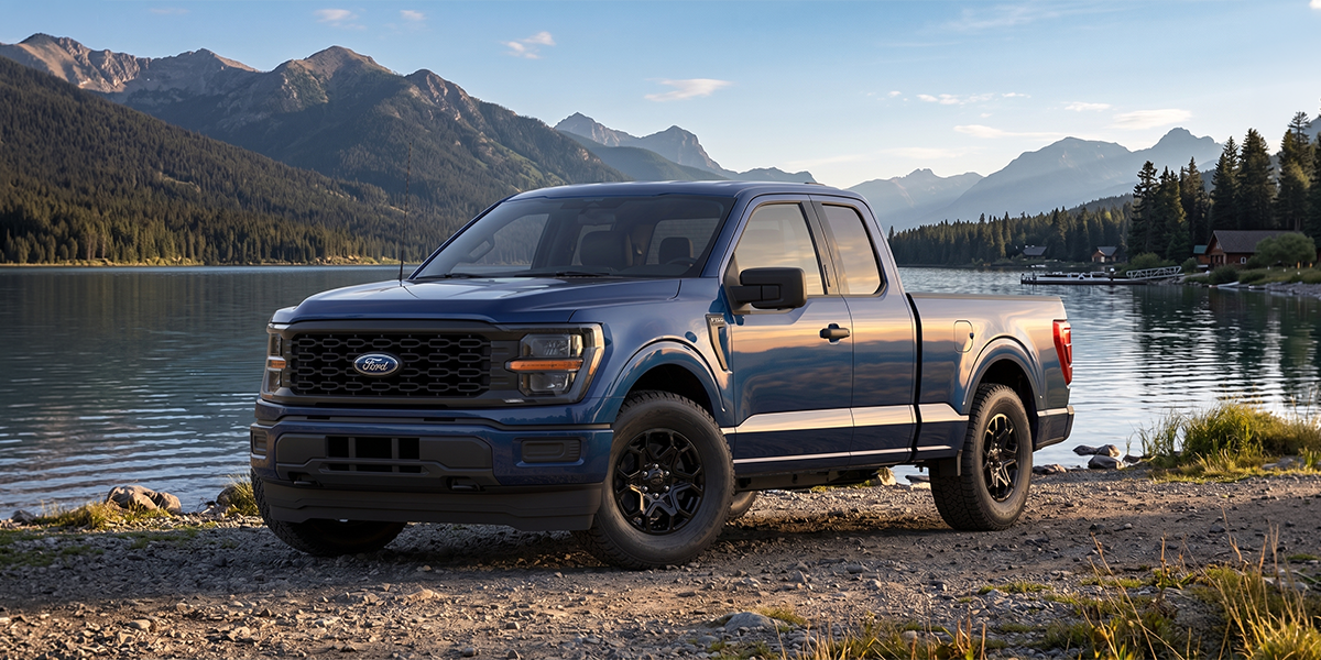 A blue Ford F-150 pickup truck parked by a tranquil lake with mountains in the background, highlighting durability and outdoor versatility.