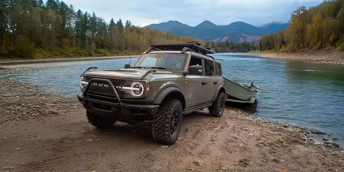A rugged off-road vehicle parked on a riverbank with mountains in the background, showcasing durability and adventure readiness for outdoor enthusiasts.