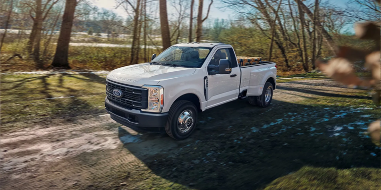 A white 2026 Ford F-150 parked on a dirt trail surrounded by trees, highlighting ruggedness and suitability for outdoor activities and work — available at MSA Ford.