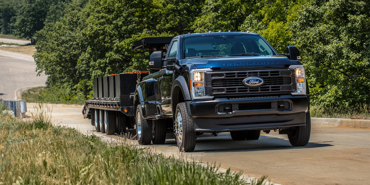 A black 2026 Ford Super Duty with a trailer on a rural road, showcasing durability and versatility for commercial purposes at MSA Ford.