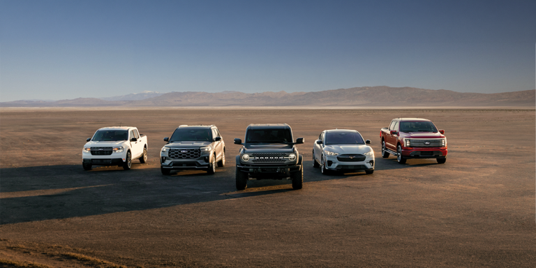 A row of five 2026 Ford trucks and SUVs parked on open terrain with mountains in the distance, showcasing the wide vehicle selection at MSA Ford.